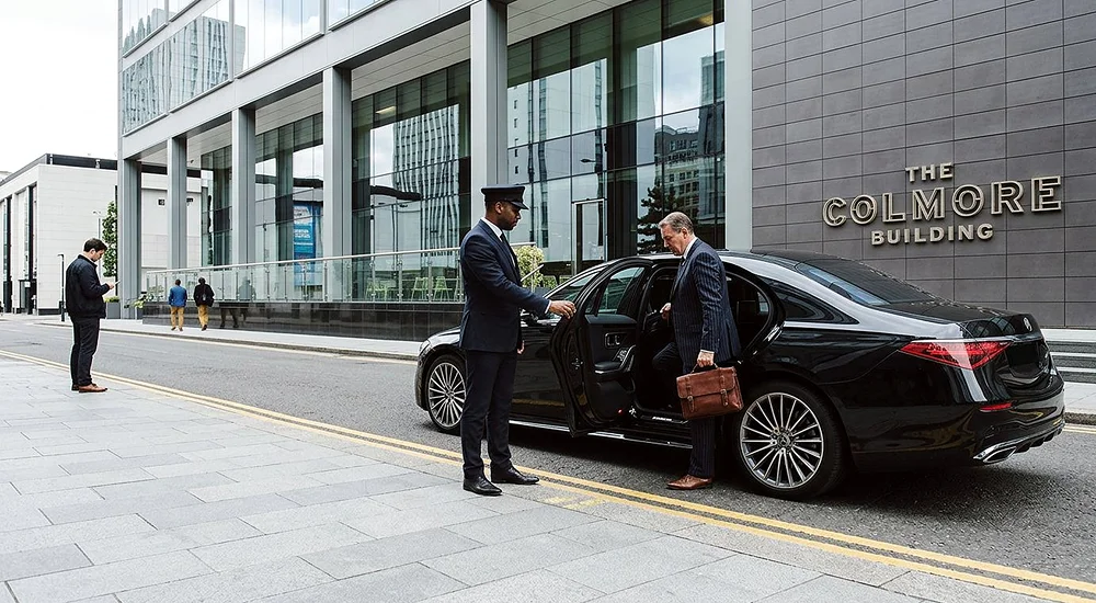 Chauffeur holding a car door open for a business traveller outside a Birmingham office